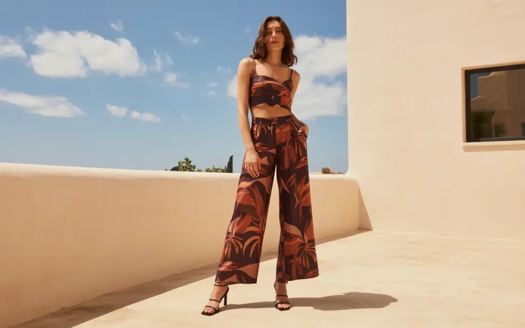 Woman wearing a bold tropical-print matching co-ord set with wide-leg trousers and a sleeveless cropped top paired with barely-there strappy heeled sandals on a sunny outdoor terrace